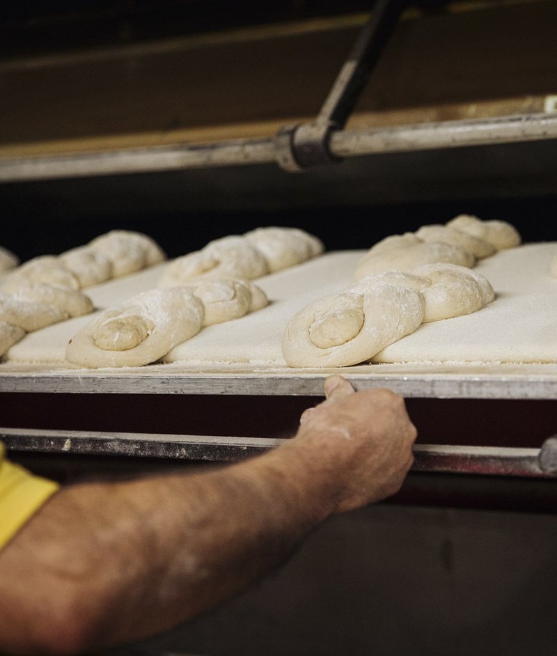Brotteige, auf Blech, werden in Holzofen geschoben